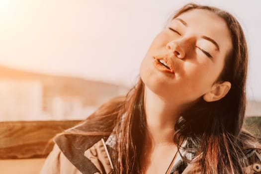 A young woman with long brown hair is pictured with closed eyes. She is wearing a brown jacket.
