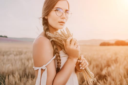 A woman is holding a bunch of wheat in her arms. The wheat is dry and brown, and the woman is wearing a white dress. The scene is set in a field, and the woman is posing for a photo