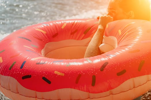 A young woman relaxes in a pink donut-shaped pool float on a sunny day. The float is wet and the woman's face is not visible.
