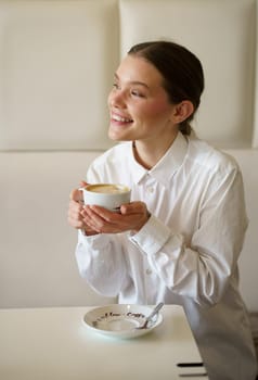 Vertical photo of a successful businesswoman smiling while enjoying morning coffee in a cafeteria