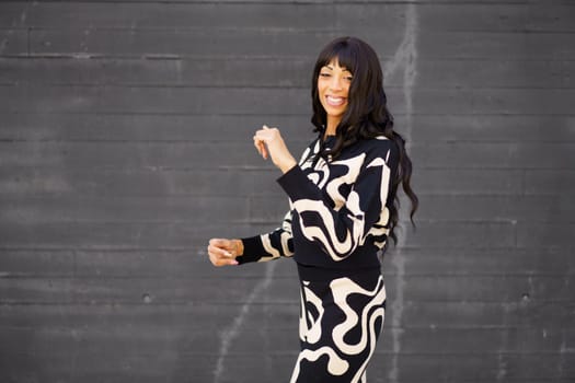 Happy confident female hispanic artist in black and white modern clothes dancing in the city