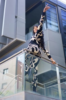 Vertical low angle view of a chic woman pointing the horizon from a rail in a skyscraper