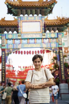 Teenage girl posing with her arms crossed at one of the entrance gates of Chinatown in London, UK.