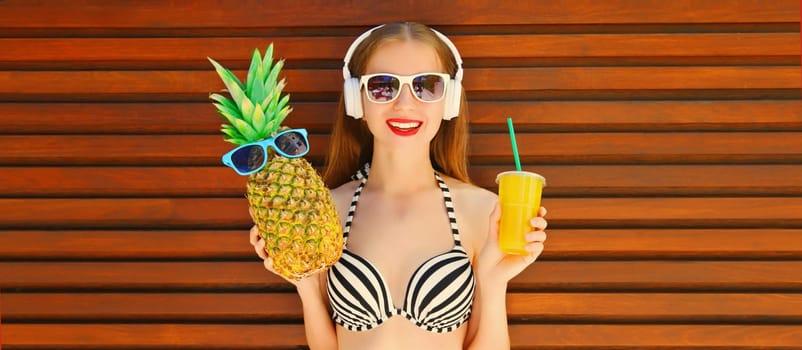 Summer portrait of happy smiling young woman listening to music in headphones with fresh cup of juice, pineapple and sunglasses