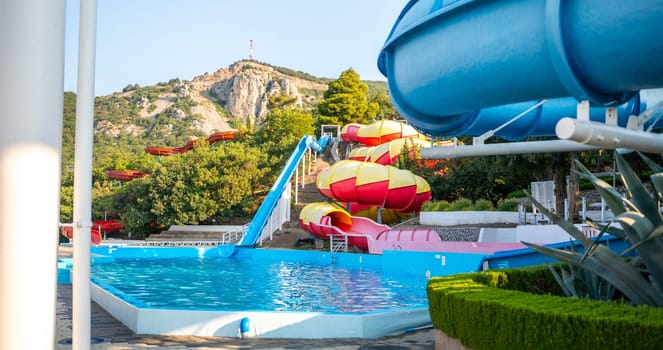 A water park with two blue and red waterslides ending in a blue pool. Green bushes and trees are in the background.