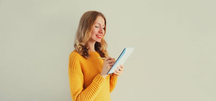 Portrait of young caucasian woman writing down memories in notebook diary on gray background