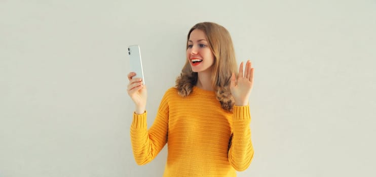 Happy smiling young woman taking selfie with phone or talking on video call waving hand on white