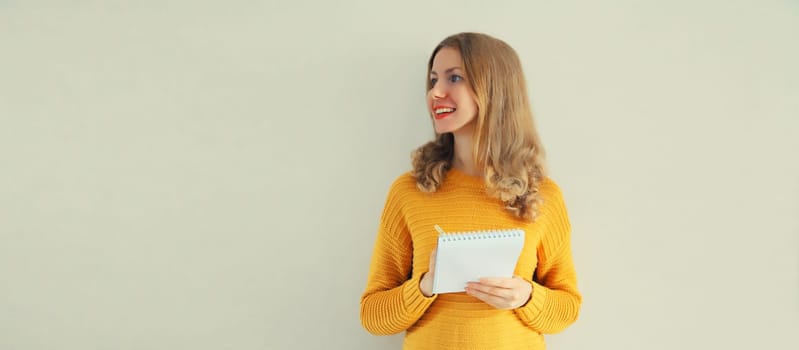 Portrait of young caucasian woman writing down memories in notebook diary on gray background