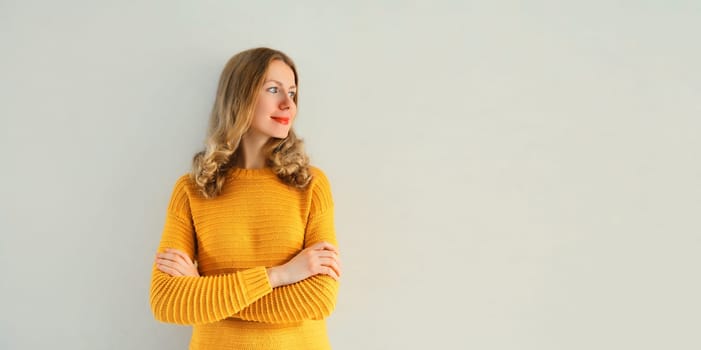 Beautiful young woman in yellow knitted sweater with crossed arms looking away on gray background