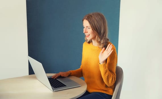 Happy young woman working with laptop welcomes communicates via video call sitting at the desk in the room at home