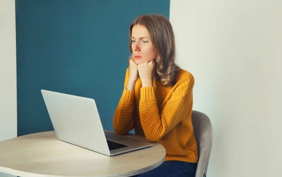 Sad young woman working with laptop sitting at the desk in the room at home