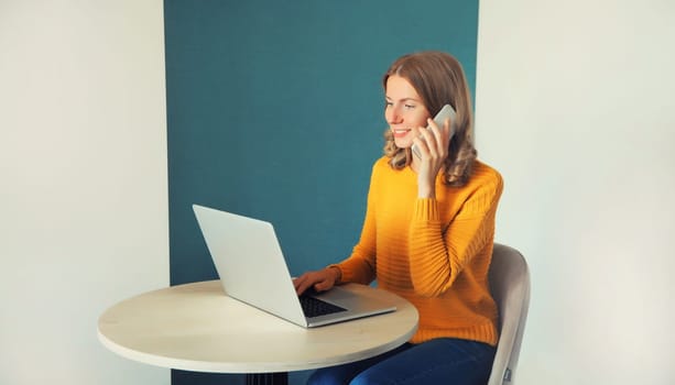 Modern young woman working with laptop and calling on smartphone sitting at the desk in the room at home