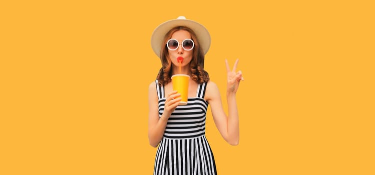 Summer portrait of beautiful young woman drinking juice in hat, striped dress on orange background