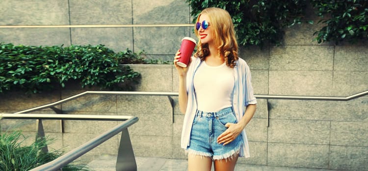 Beautiful modern smiling young woman drinking coffee looking away in the city