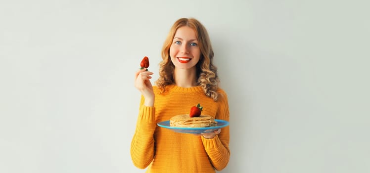 Cooking, happy smiling young woman housewife holding plate with stack of pancakes with strawberries