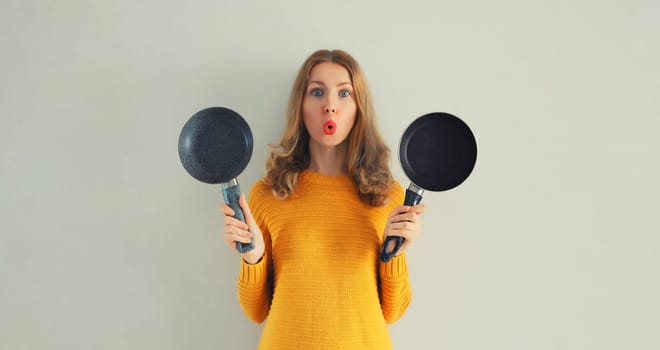Cooking mood, portrait happy smiling young woman housewife with empty frying pan on gray background