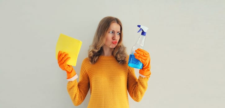 House cleaning concept - housewife or cleaner, unhappy sad woman in rubber protective gloves holding dry microfiber rag and detergent spray bottle