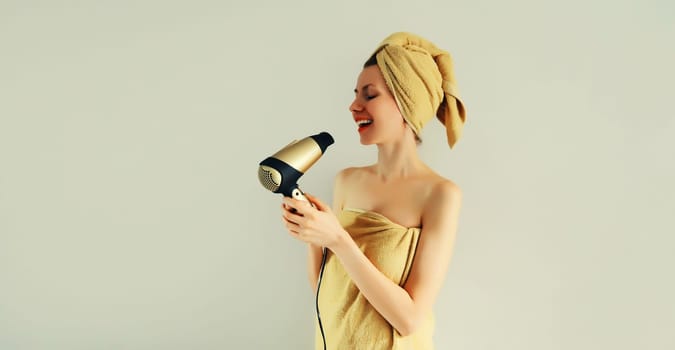 Portrait of happy smiling young woman drying wet hair in wrapped bath towel after taking a shower