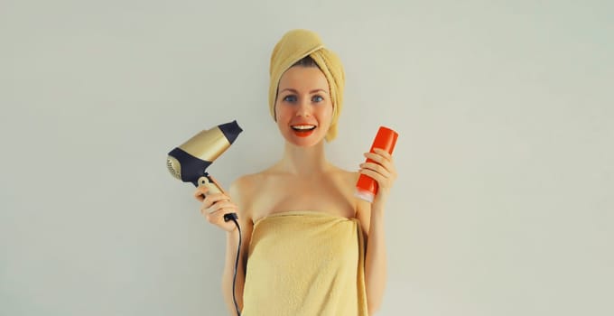 Happy smiling woman drying wet hair in bath towel holding bottle of shampoo after taking a shower