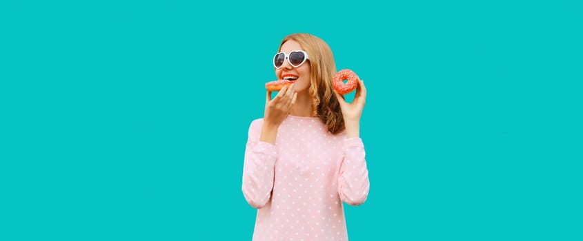 Happy cheerful young woman with sweet donut having fun in heart shaped glasses on blue background