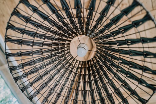 Close up of a wicker lamp shade with a light bulb inside, creating a geometric pattern.