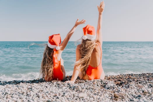 A mother and daughter in red swimsuits and Santa hats are enjoying the beach on a sunny day.