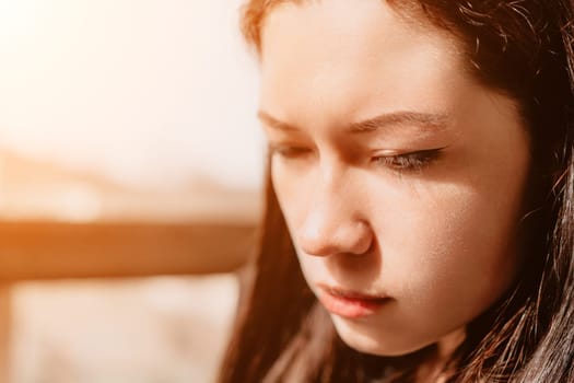 A close-up portrait of a young woman with long brown hair, gazing downward in a contemplative mood, bathed in warm sunlight.