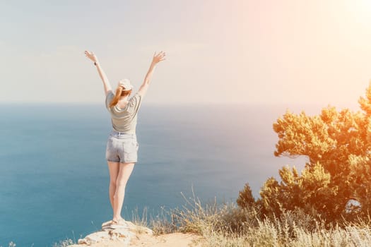 A woman with arms raised in triumph stands on a cliff overlooking a vast blue sea, with a sun-drenched sky above.
