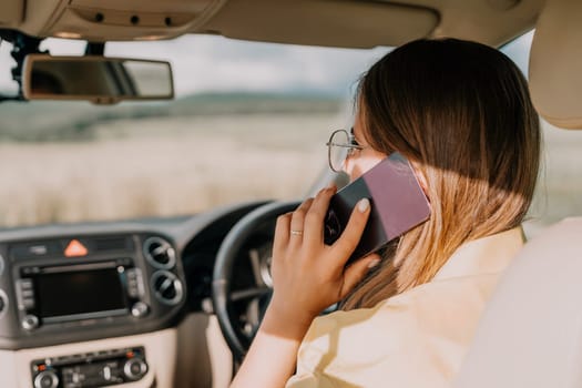 A woman in a yellow shirt is talking on the phone while driving a car. The car is in motion and the view outside the window is blurred.