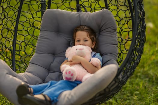 A joyful child cherishes a serene moment while swinging gently in a cozy swing, hugging a fluffy teddy bear tightly
