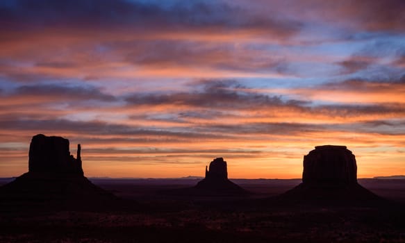 Silhouette of Monument Valley's iconic Mittens and Merrick Butte rock formations against a pink and orange dusk sky in Arizona, USA. Captures the stunning beauty of the desert landscape during sunset.