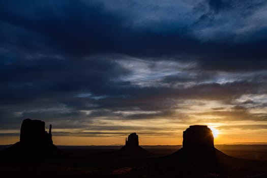 Captivating sunrise at Monument Valley, showcasing the iconic Mittens and Merrick Butte in silhouette. The lens flare adds a dramatic touch to the morning sky, highlighting the beauty of Arizona, USA.