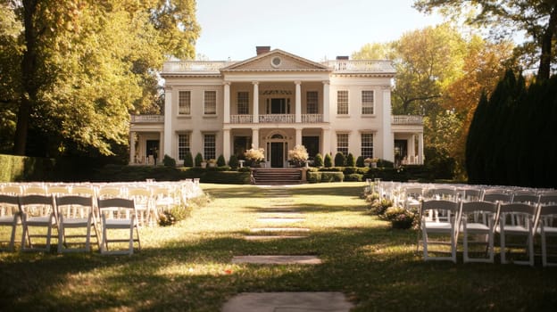 A beautiful outdoor wedding ceremony is set up in front of a historic mansion with white chairs arranged on a manicured lawn, framed by vibrant autumn foliage.