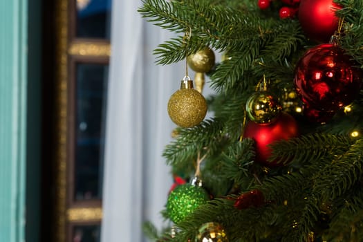 Close-up cropped shot of beautiful Christmas tree decorated with festive balls and celebration warm lights at home, selective focus.