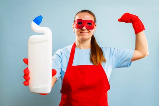 Woman in super hero's red mask flexing muscles while holding a cleaning product. Studio shot for design and print. Home cleaning and strength concept
