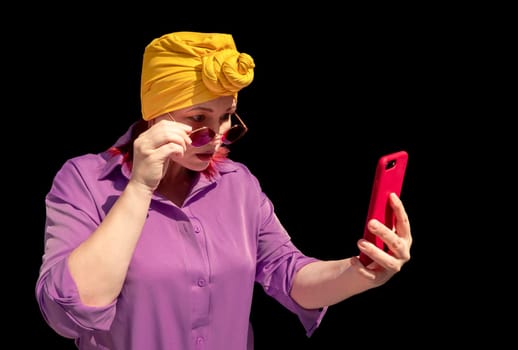 Happy and funny cool lady with fashionable clothes on dark background look peering closely to the phone with different emotions - adult asian with extravagant style. isolated on black background