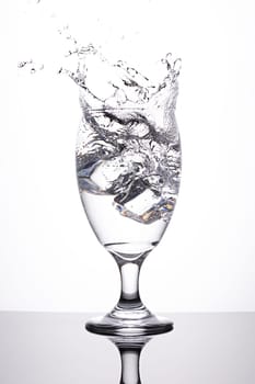A studio photo of ice being dropped into a glass of water against a white background.