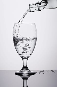 A studio photo of pouring water from a bottle into a glass against a white background.