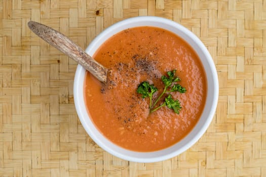 A studio overview photo of a bowl of tomato soup with a sprig of parsley on top.