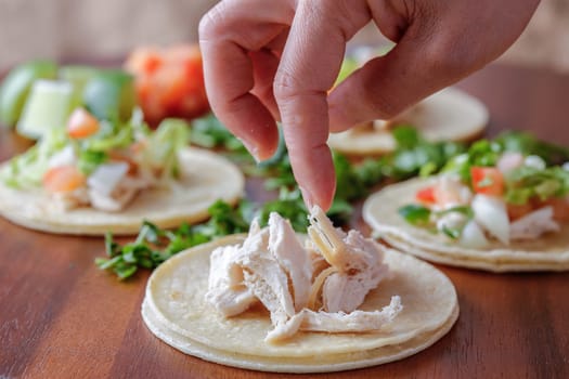 Putting pieces of chicken on a small street taco on a wooden board.