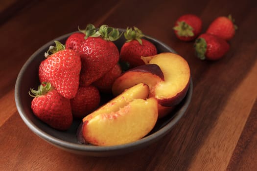 A studio photo of a bowl of fresh strawberries and sliced peaches.