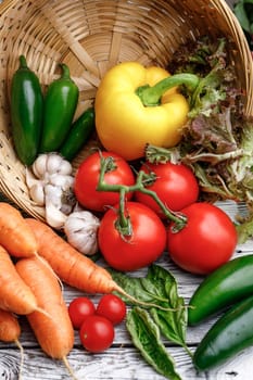 Assorted vegetables and basil in a basket on a wooden table.