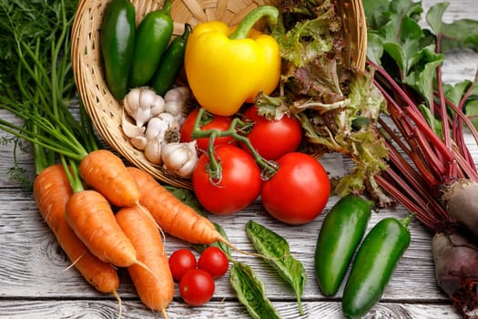 Assorted vegetables and basil in a basket on a wooden table.