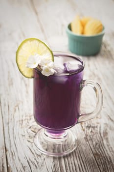 A refreshing glass of butterfly pea flower tea with ice and a lime.