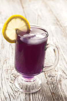 A refreshing glass of butterfly pea flower tea with ice and a lemon slice.