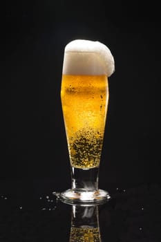 A close up uof a glass of beer against a black background starting to overflow.