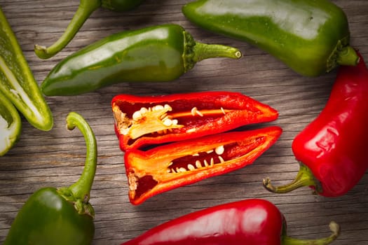 An overview of whole and sliced red and green peppers on wood.