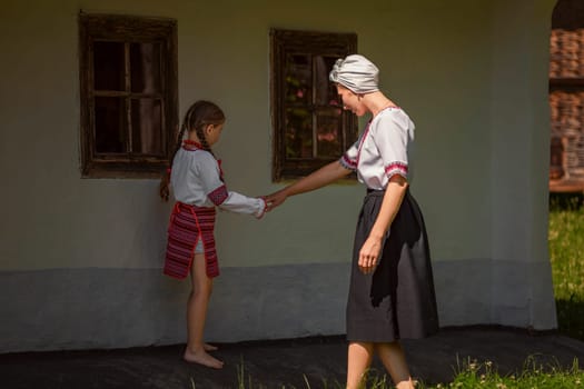 In front of a house, a woman and a little girl joyfully hold hands, possibly enjoying a special event. The scene captures happiness and warmth