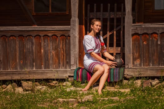 A woman in beautiful traditional attire stands gracefully by a rustic house, showcasing cultural heritage