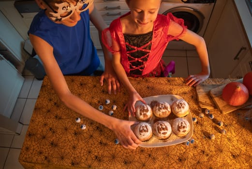 girl and brother trying buns with ghost images, they are dressed in Halloween costumes, enjoying holiday treats in decorated dark kitchen, warm cozy atmosphere, holiday mood,